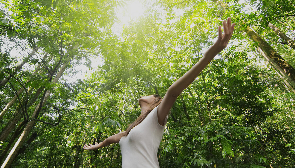 Vrouw in het bos, armen gespreid in vrijheid en verbondenheid met de natuur